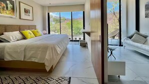 Un dormitorio moderno con una cama grande, un ventilador de techo y vistas al exterior a través de amplios ventanales.