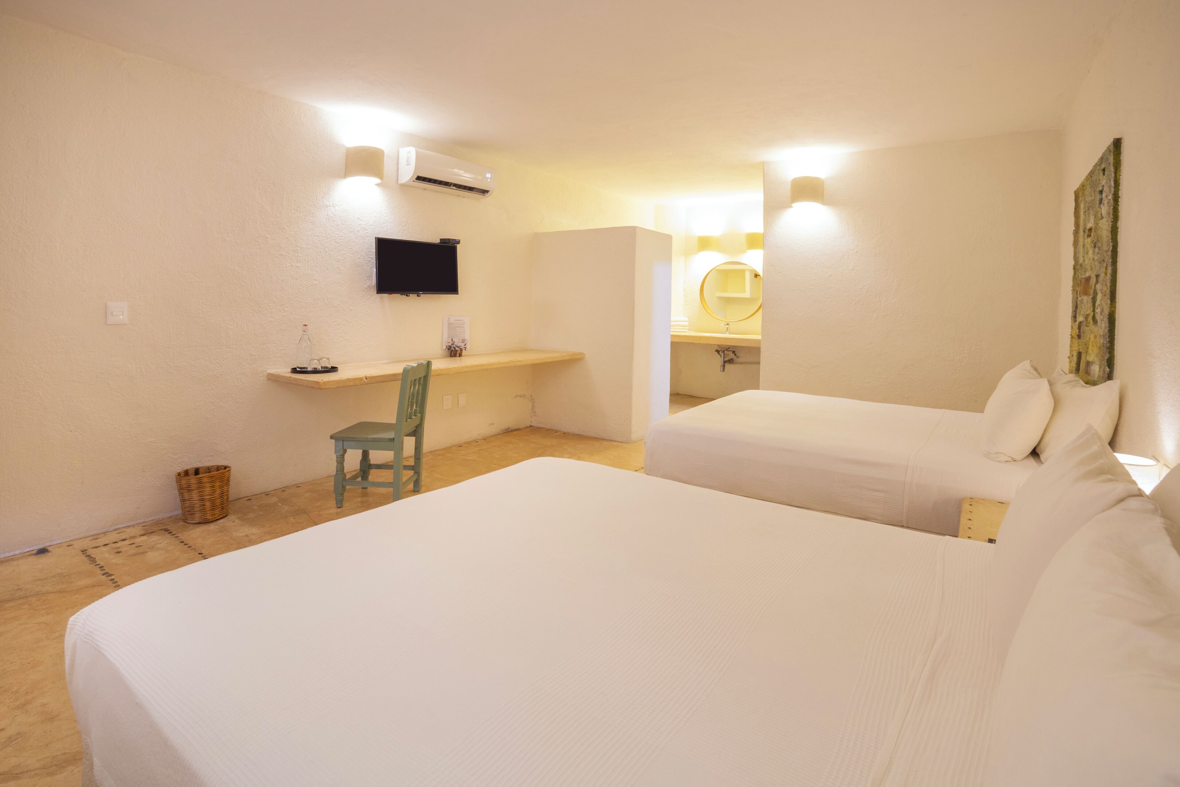 A hotel room with two beds, a desk, a chair, a small table, and a wall-mounted TV.