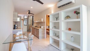Una cocina moderna con una mesa de comedor de vidrio, sillas blancas y un estante blanco decorado con objetos.