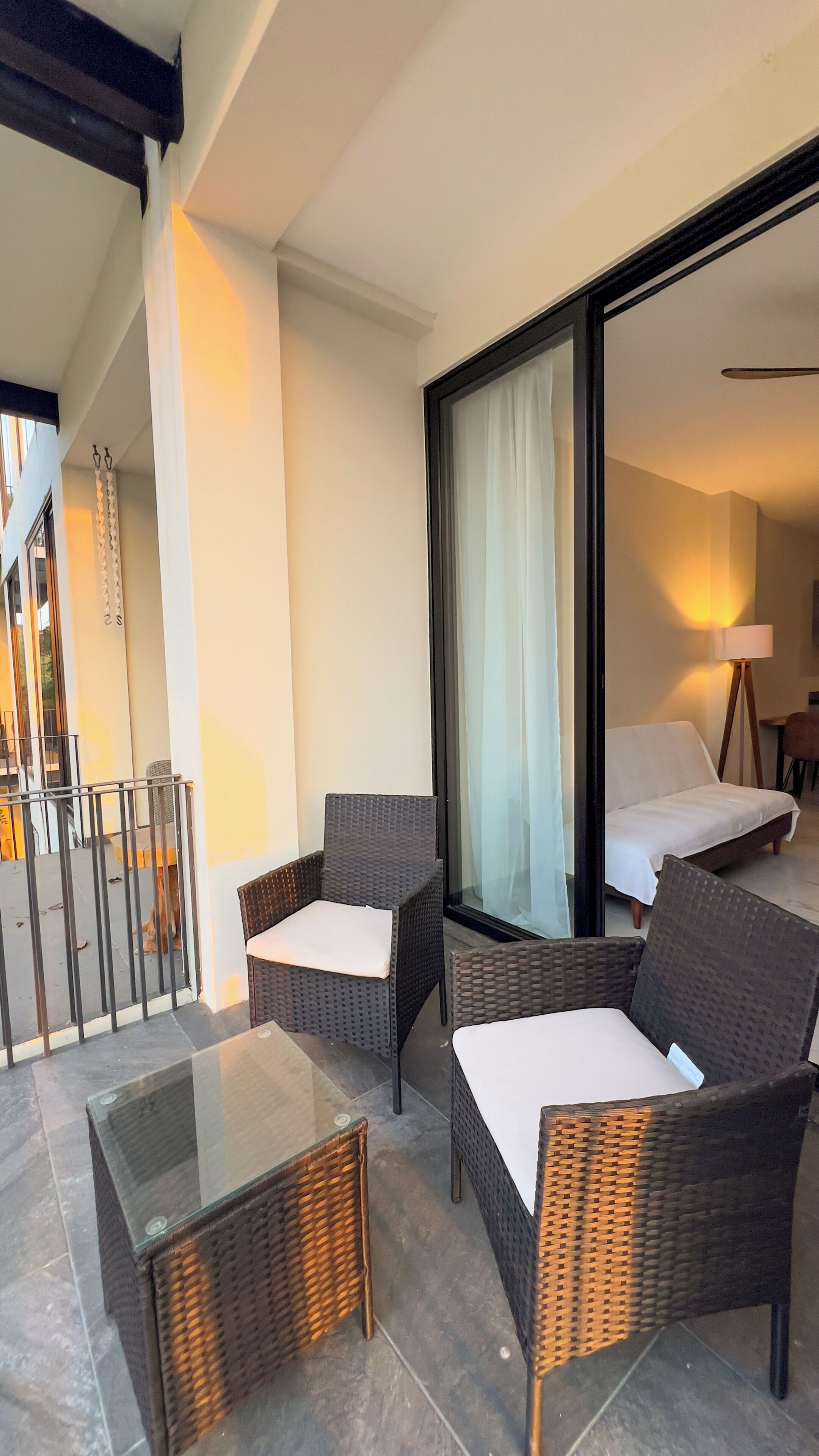 A balcony with wicker furniture, a glass table, and a view of the interior.