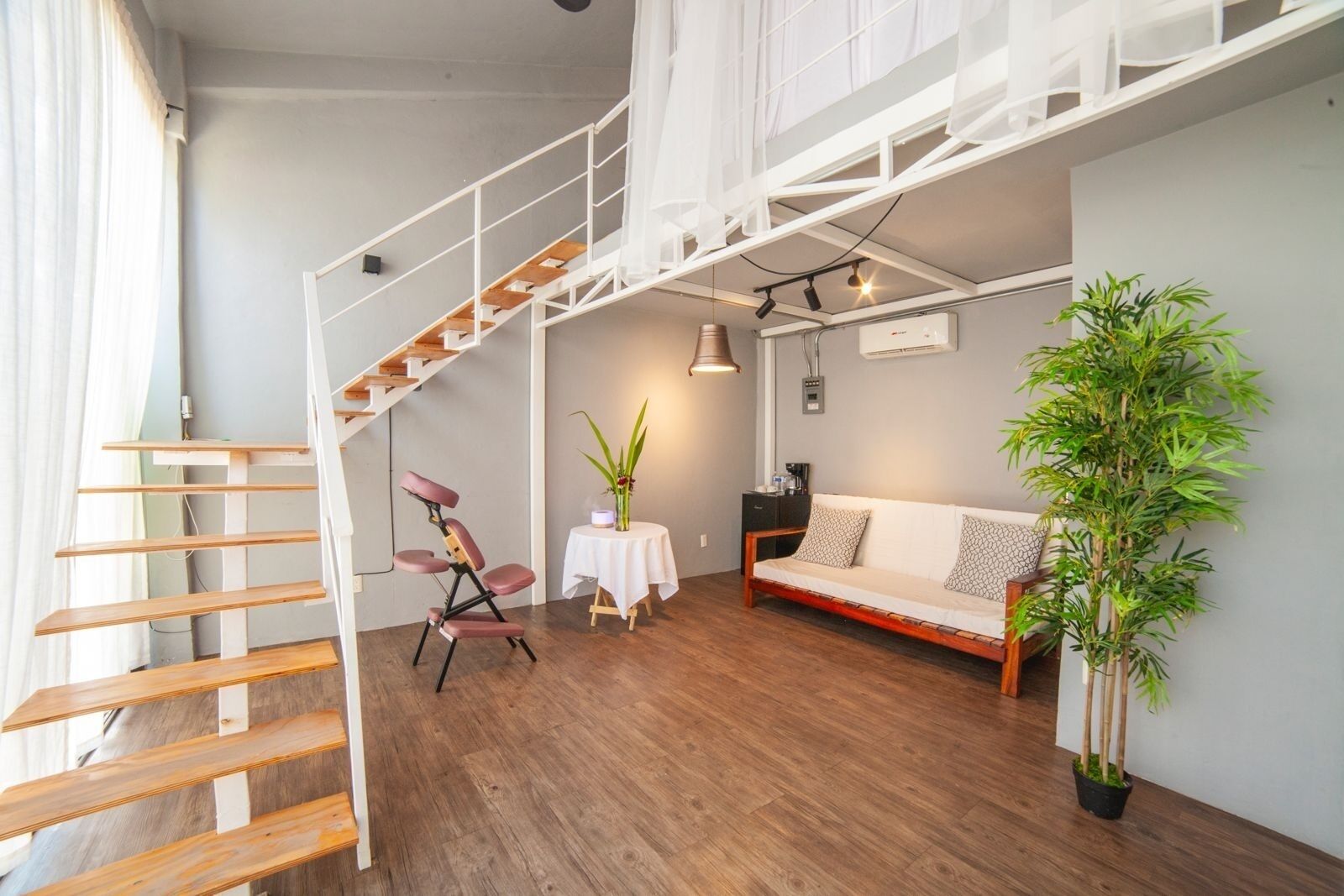 A loft-style room with a wooden staircase, a sofa, a table with a plant, and a potted bamboo plant.