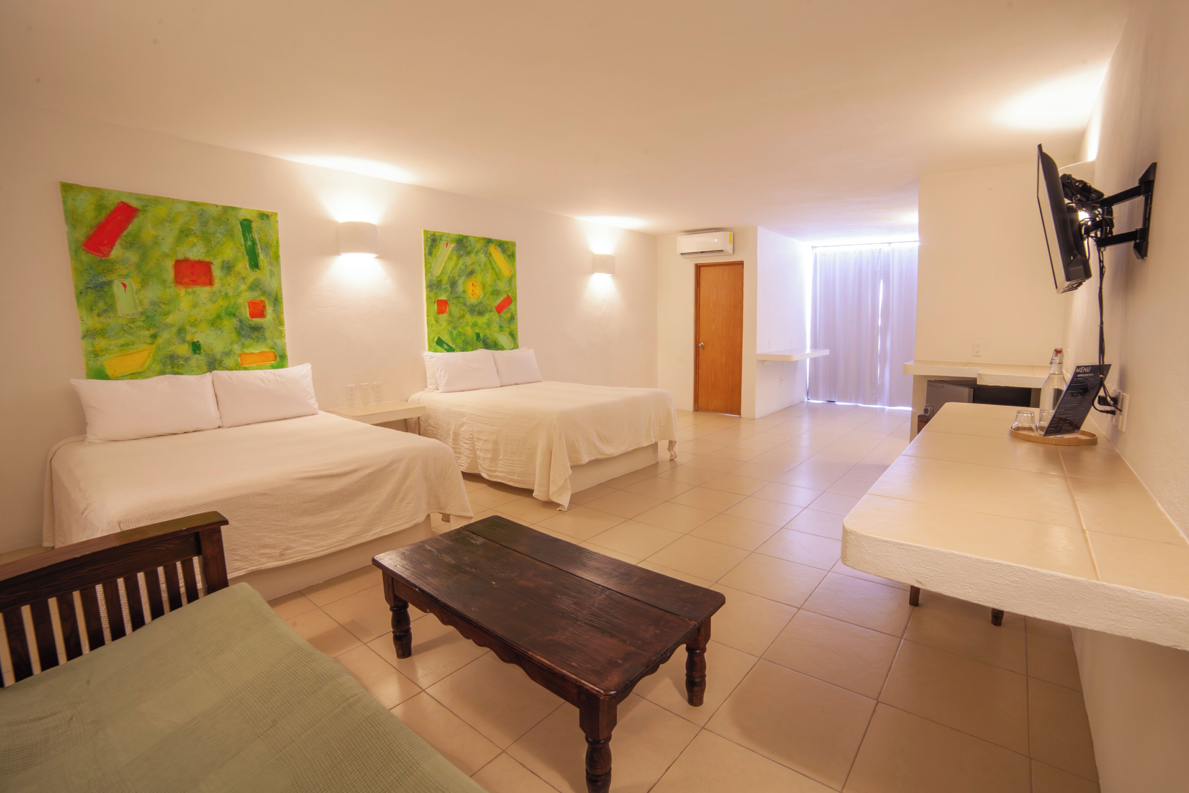 A hotel room with two beds, a wooden table, a TV, and artwork on the walls.