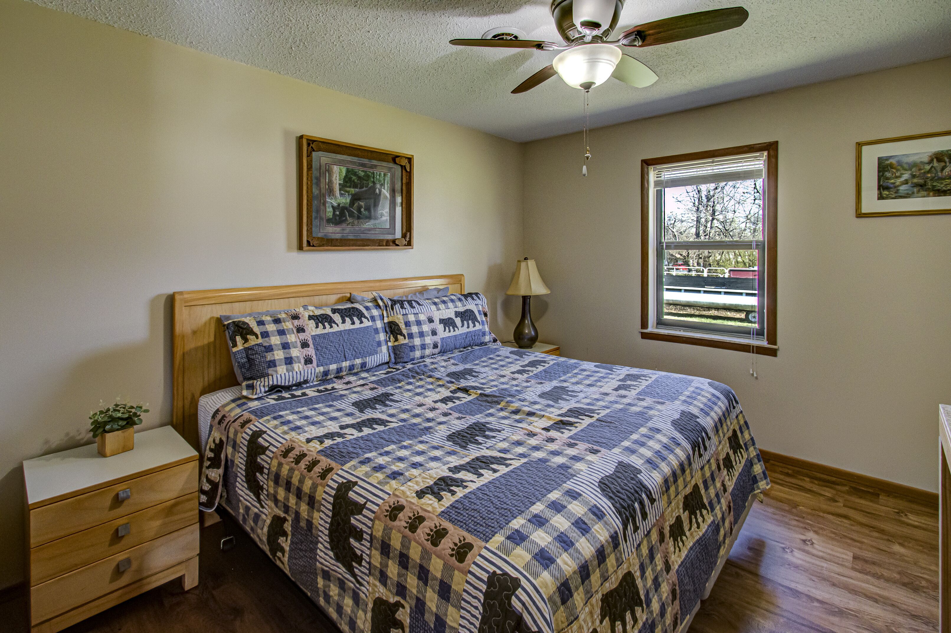 A bedroom with a bed, a nightstand, a lamp, a ceiling fan, and two windows.