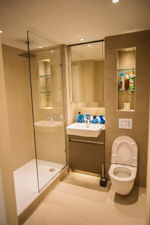 A modern bathroom with a glass-enclosed shower, a sink with toiletries, and a toilet. - Immaculate 2-bed Apartment in London (London)