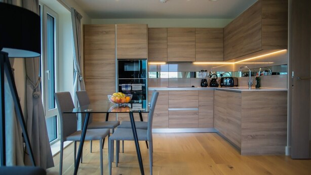 Een moderne keuken met houten kastjes, een glazen eettafel met stoelen en een fruitschaal.