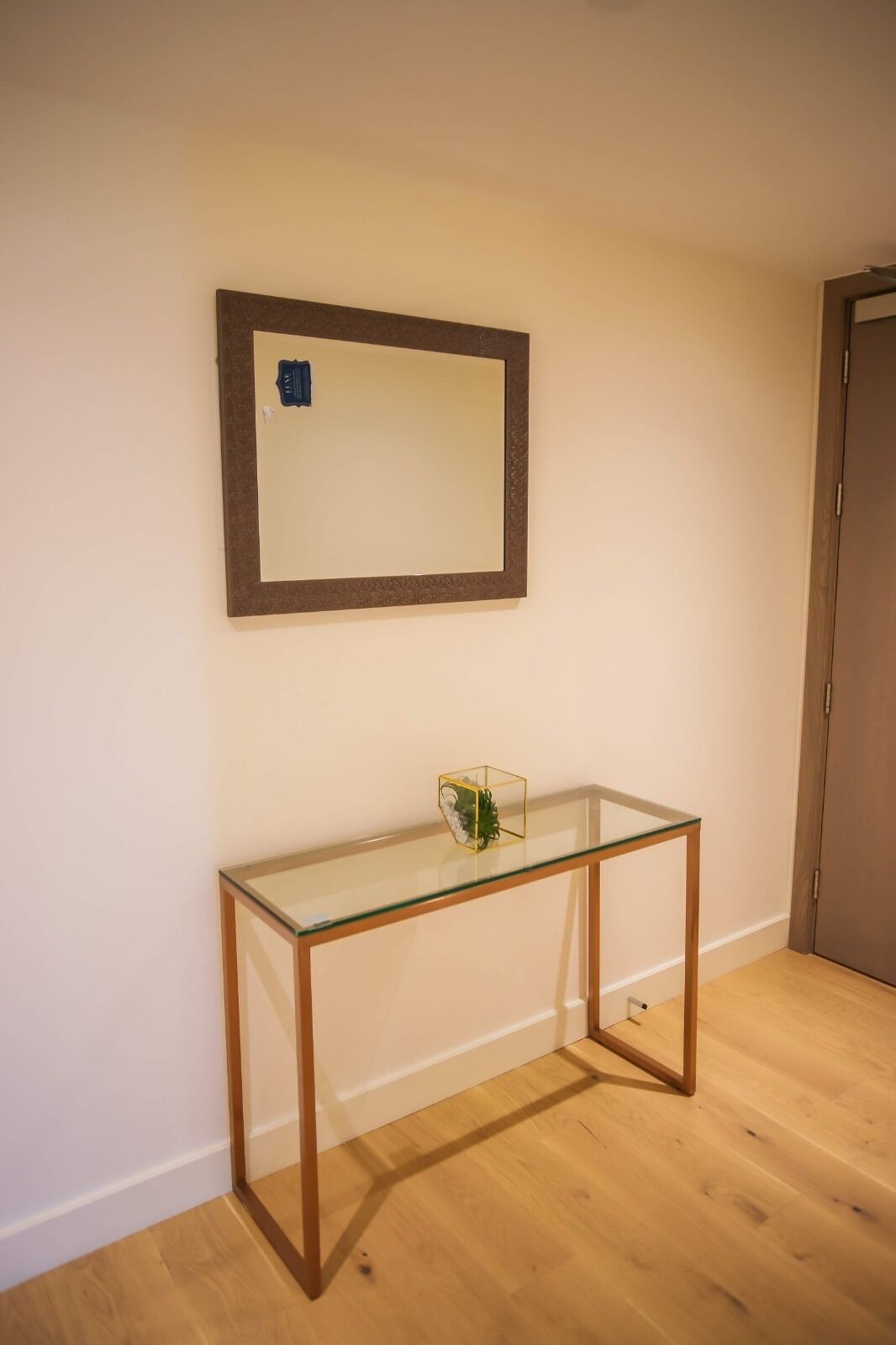 Een kamer met een tafel met glazen blad, een houten vloer en een deur op de achtergrond.