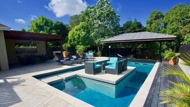 A rectangular swimming pool with a wooden deck and lounge chairs. - Adehya the Villa (Duncans)