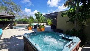 A hot tub in a backyard with a wooden deck, potted plants, and a clear blue sky. - Adehya the Villa (Duncans)