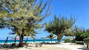 A beach with trees, a swing set, and umbrellas. - Adehya the Villa (Duncans)