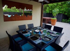 Un coin repas avec une table en verre dressée pour six personnes, entourée de chaises en osier agrémentées de coussins bleus.