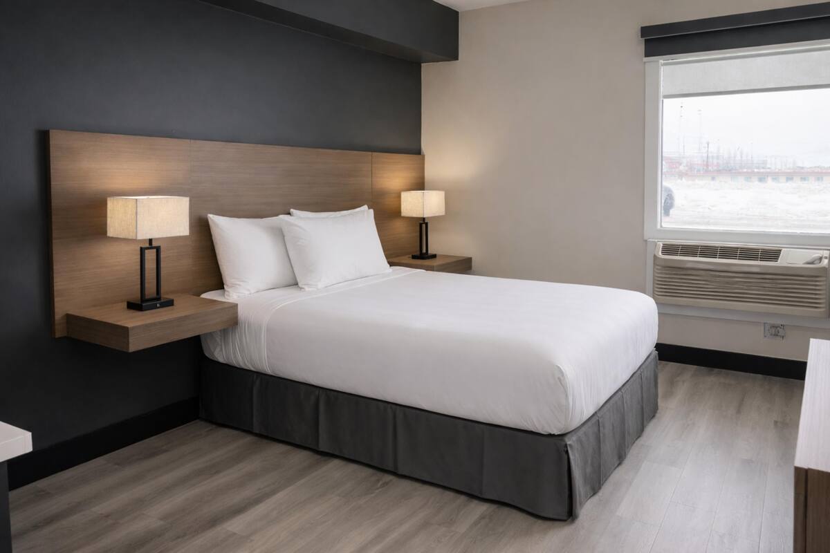 Une chambre d’hôtel comprenant un lit, deux lampes de chevet, une fenêtre avec stores et un climatiseur fixé au mur.
