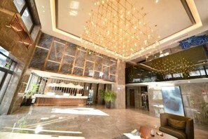 A spacious lobby with a reception desk, a chandelier, and a large window.
