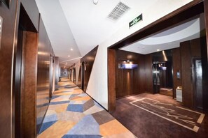A hotel corridor with a patterned carpet, wooden walls, and a modern elevator.