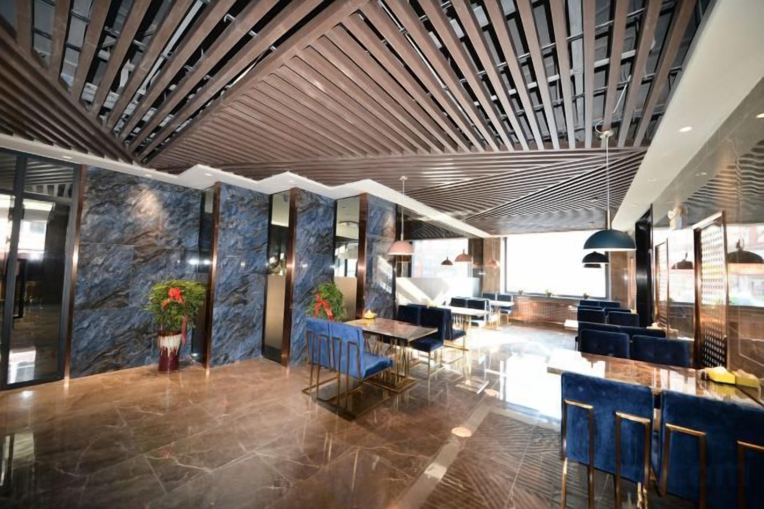 A modern lobby with a high ceiling, marble walls, and a seating area with blue chairs.