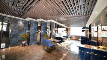 A modern lobby with a high ceiling, marble walls, and a seating area with blue chairs.