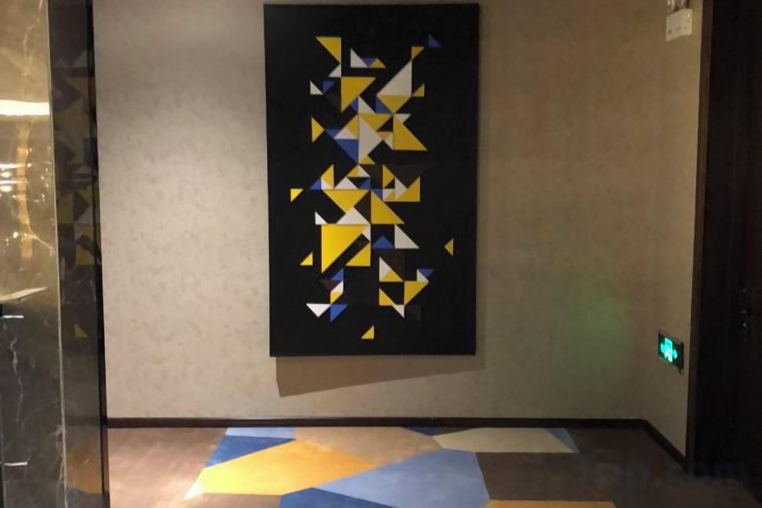 A hallway with a geometric art piece on the wall and a patterned floor.