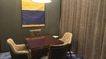 A room with a wooden table, four chairs, a lamp, a large abstract painting, and a curtain.
