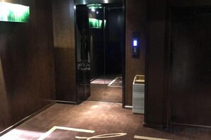 Un pasillo con ascensor, piso alfombrado y una lámpara en la pared.