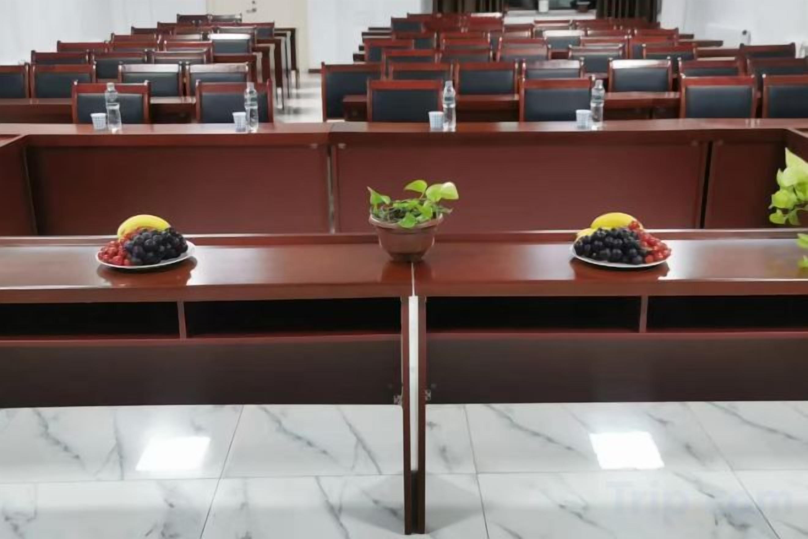 Un salón de conferencias con filas de sillas y mesas, algunas con botellas de agua y fruteros.