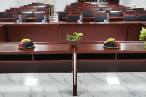 A conference room with rows of chairs and tables, some with water bottles and fruit bowls.