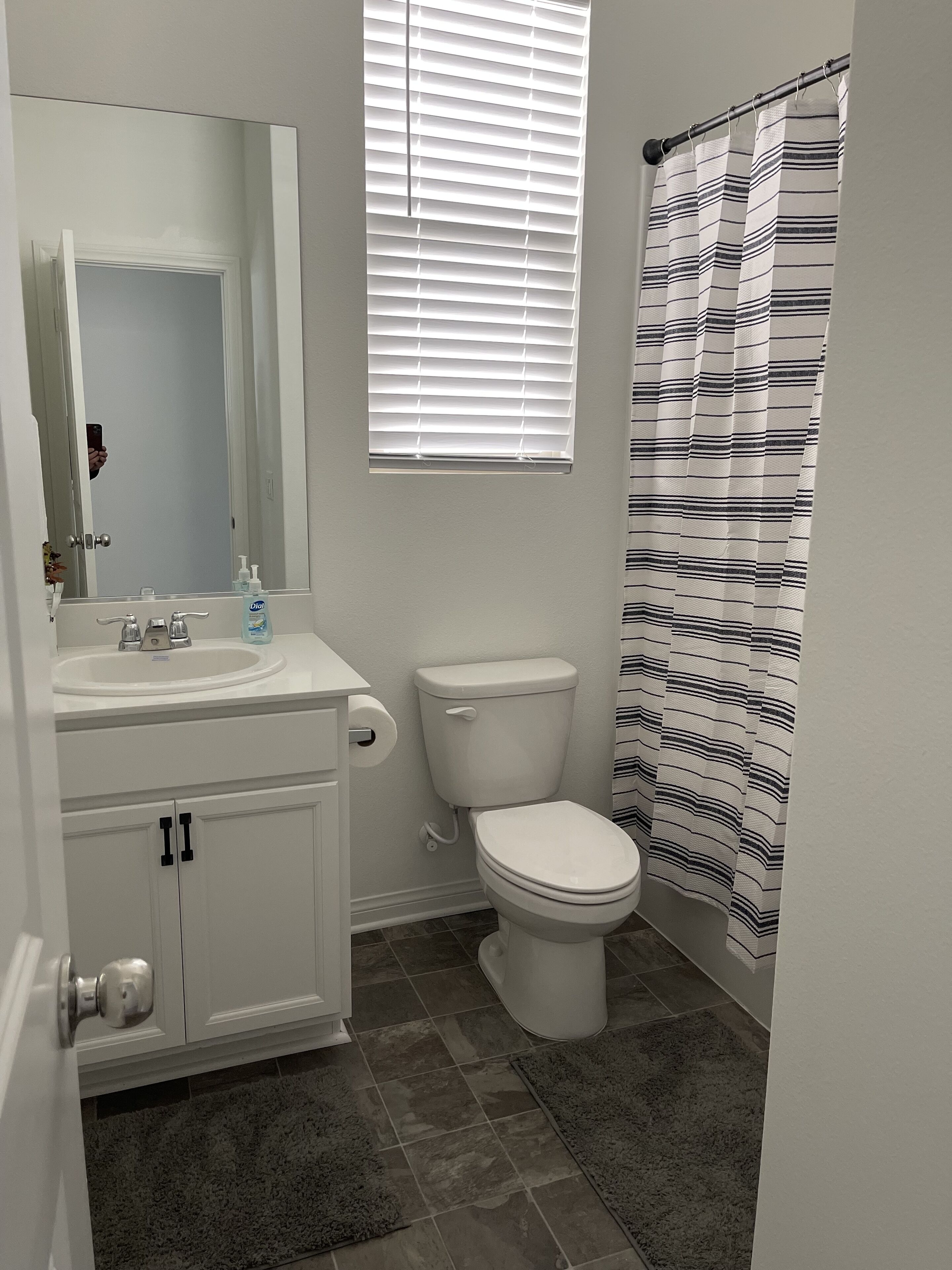 A bathroom with a white sink, mirror, toilet, and striped shower curtain.