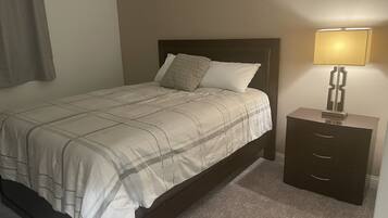 A neatly made bed with a patterned bedspread and pillows, a bedside table with a lamp, and a carpeted floor.