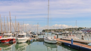 A marina with various boats docked, a pier, and a building in the background.
