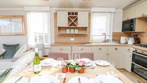 A modern kitchen with white cabinets, a built-in oven, and a dining area set for six with a table, chairs, and a flower centerpiece.