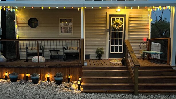 A two-story house with a porch, wooden steps, and string lights. - “SERENDIPITY” a boho inspired tiny home on wheels in country setting (Sweetwater)