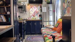 A compact, well-organized kitchen with modern appliances, a dining area with a wooden table, and a cozy sleeping area with a colorful quilt. - “SERENDIPITY” a boho inspired tiny home on wheels in country setting (Sweetwater)