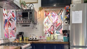 A kitchen with a microwave, stove, and refrigerator. There is a patterned window and a rug on the floor. - “SERENDIPITY” a boho inspired tiny home on wheels in country setting (Sweetwater)