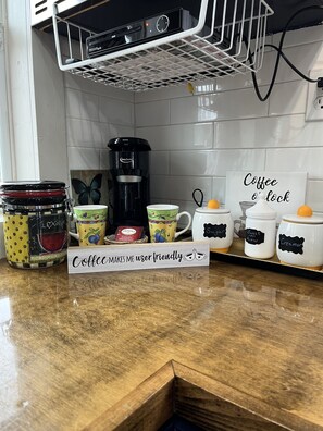 A kitchen counter with a coffee maker, mugs, and a sign that reads 'Coffee makes me user friendly.' - “SERENDIPITY” a boho inspired tiny home on wheels in country setting (Sweetwater)