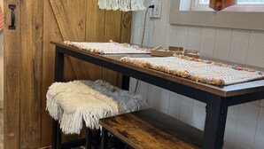 A rustic wooden room with a long table, two stools, a macramé hanging light, and a window with a curtain. - “SERENDIPITY” a boho inspired tiny home on wheels in country setting (Sweetwater)