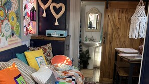 A cozy bedroom with a colorful quilted bedspread, a blue suitcase, and a macrame hanging light. - “SERENDIPITY” a boho inspired tiny home on wheels in country setting (Sweetwater)