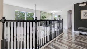 Un espacio interior amplio con piso de madera, barandal negro y grandes ventanas que dejan entrar luz natural.
