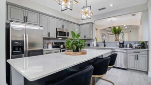 Una cocina moderna con electrodomésticos de acero inoxidable, una isla central con taburetes de bar e iluminación colgante.