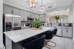 A modern kitchen with stainless steel appliances, a central island with bar stools, and pendant lighting.