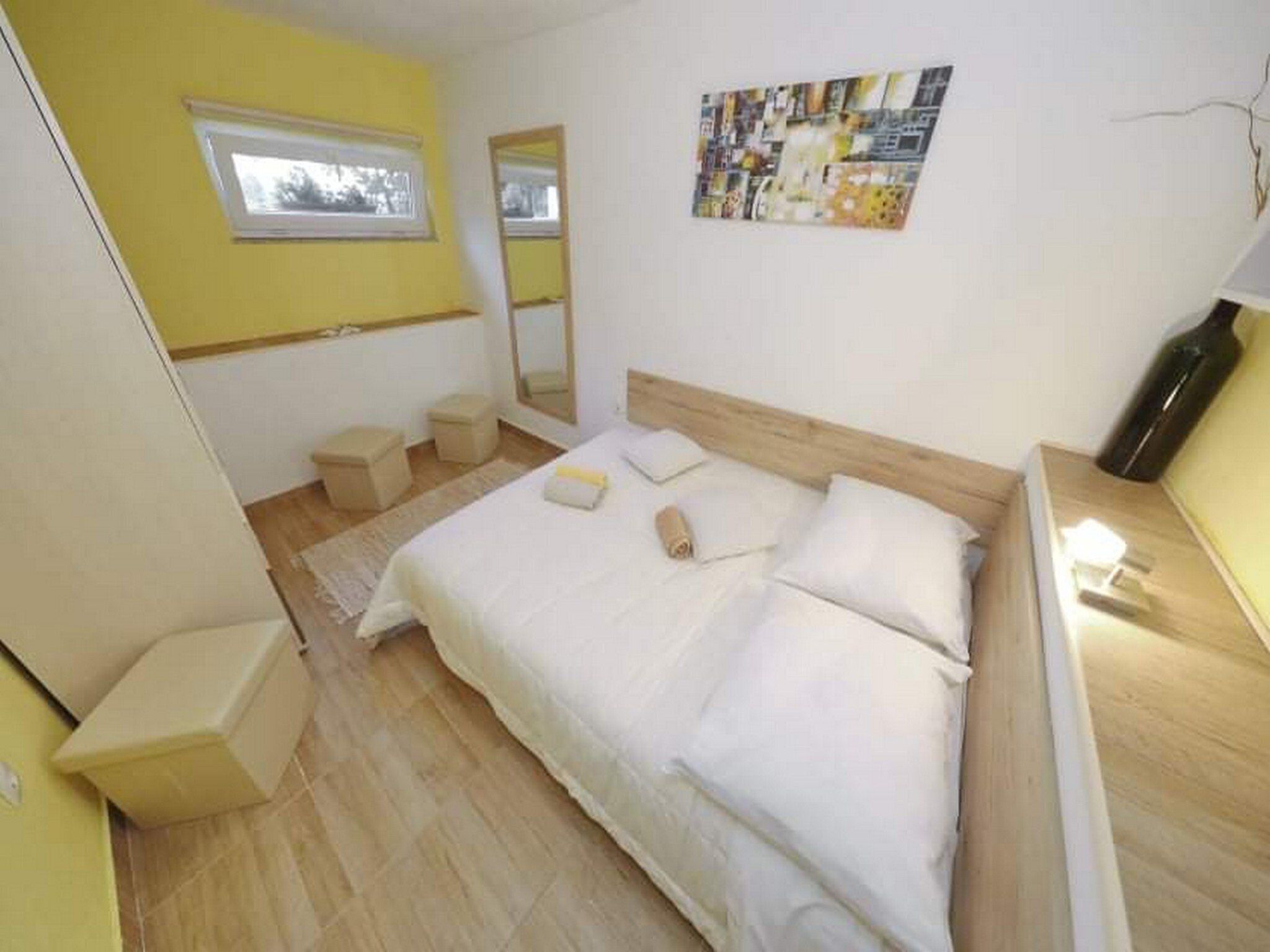 A bedroom with a bed, a window, a mirror, and a wall art piece.
