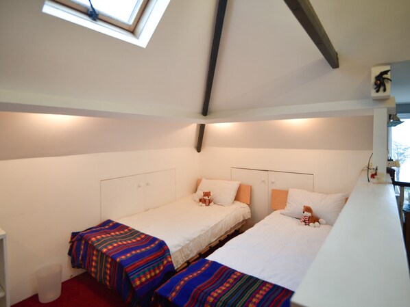 A dormitory room with two single beds, a small window, and a white wall.