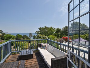 A balcony with a wicker sofa, a table with wine glasses, and a view of the sea.