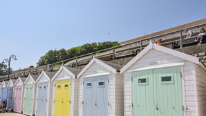 A row of colorful beach huts with numbered doors, a staircase leading to a viewing platform, and a clear sky. - Coram Cottage (Lyme Regis)
