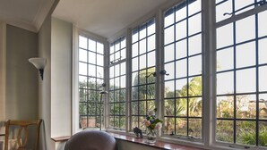 A room with a large window, a chair, and a vase with flowers on the windowsill. - Coram Cottage (Lyme Regis)