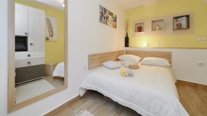 Une chambre à coucher comprenant un lit, un grand miroir, une tête de lit en bois et une étagère murale agrémentée d’objets décoratifs.