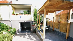 Un espace extérieur abrité, doté d’une pergola en bois, d’un coin salon avec une table et des chaises, et d’un petit jardin agrémenté de plantes en pot.