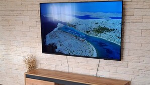 Un salon moderne avec un téléviseur à écran plat fixé à un mur en briques, un meuble TV en bois doté de tiroirs et un coussin décoratif à motifs sur un canapé blanc.