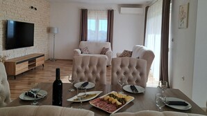Un salon doté d’un téléviseur à écran plat, de deux canapés, d’une table basse en bois sur laquelle sont disposés des assiettes de nourriture et des verres à vin, et d’un mur à la texture de pierre.
