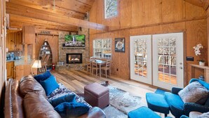 Un interior de cabaña acogedor con chimenea de piedra, pisos de madera, un sofá de cuero y una zona de comedor.