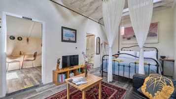 A bedroom with a four-poster bed, a bedside table with a vase of flowers, a television, and a bookshelf.