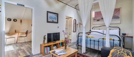 A bedroom with a four-poster bed, a bedside table with a vase of flowers, a television, and a bookshelf.