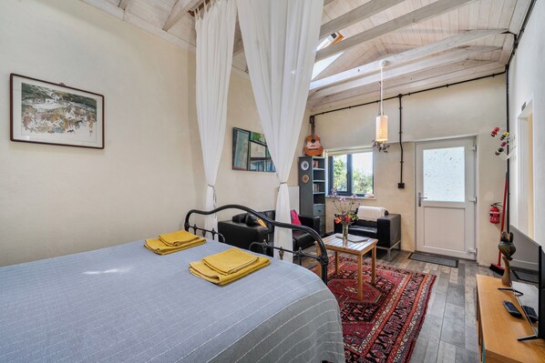 A bedroom with a bed, a small table, a chair, a bookshelf, and a window.